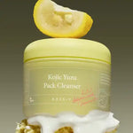 Conceptual stack of Axis-Y cleanser jar on white foam, under a yuzu slice, with olive-green background.