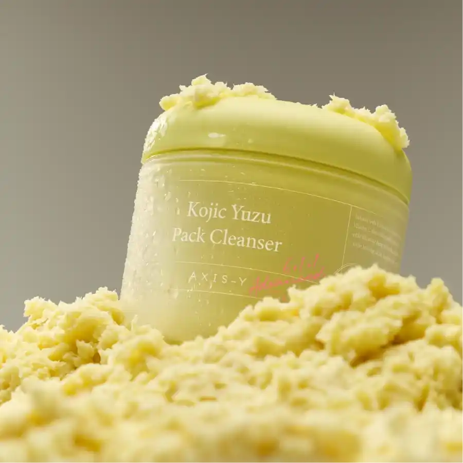 Axis-Y Kojic Yuzu cleanser jar resting on a fluffy, light-yellow soufflé texture in clear lighting.
