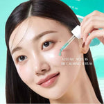 A woman applying the turquoise Medicube Calming Serum to her cheek using a dropper.