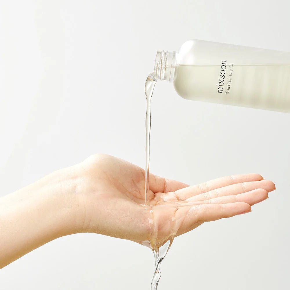 Clear Mixsoon Bean Cleansing Oil being poured into a hand to show lightweight texture.