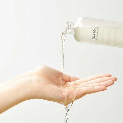Clear Mixsoon Bean Cleansing Oil being poured into a hand to show lightweight texture.