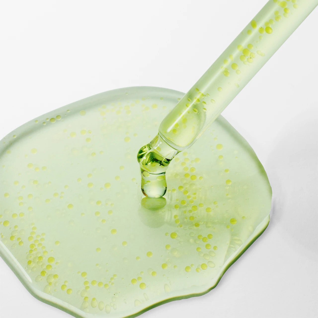 Dropper applying clear green Purito Azelaic Acid serum onto a smooth surface.