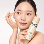 A woman applying a drop of milky Purito Oat PDRN toner directly to her cheek.