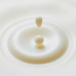 Close up of a milky white liquid drop splashing into a pool of toner.