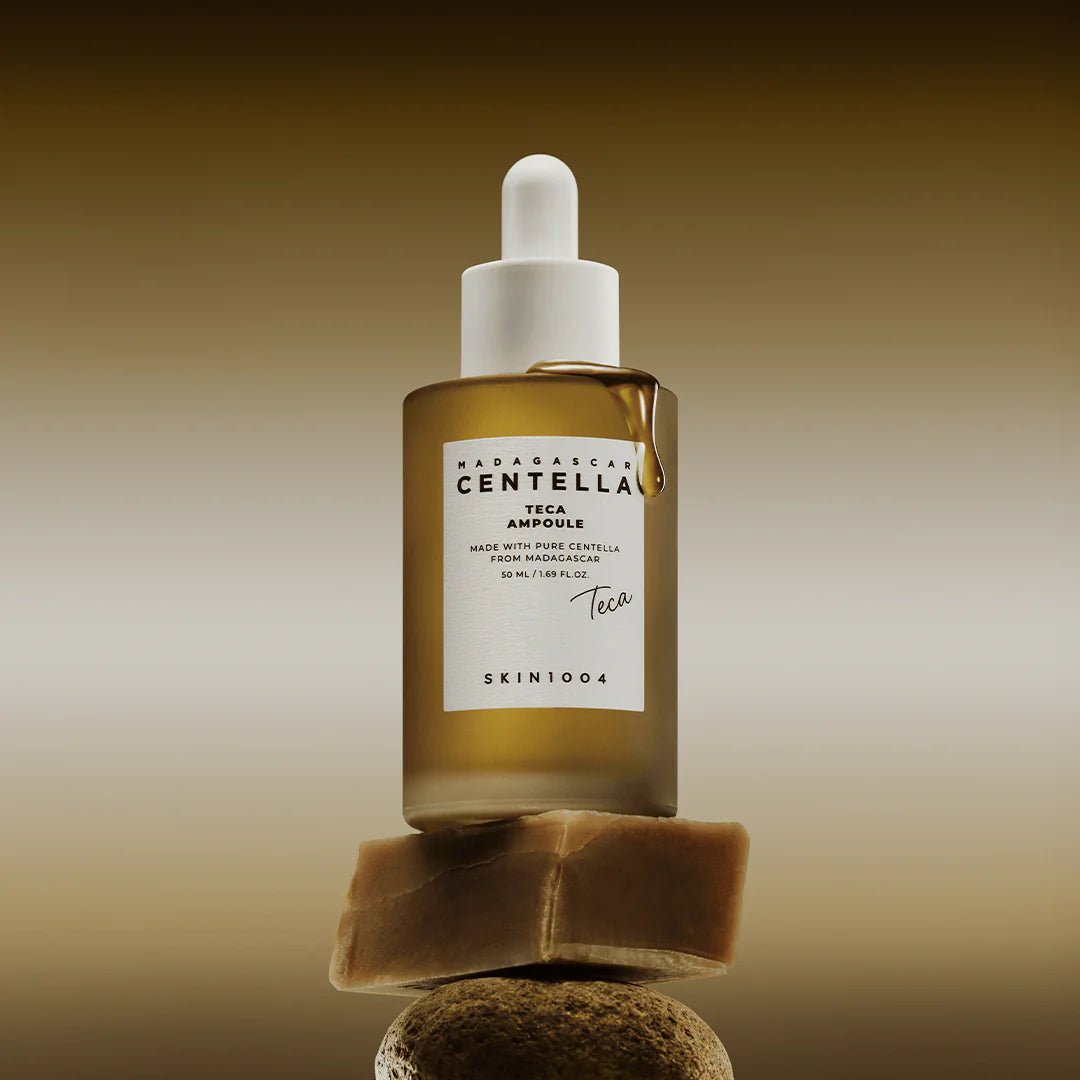 Skin1004 Centella Teca Ampoule bottle balanced on a natural stone with a golden liquid drip.
