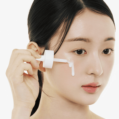 A woman applying the white milky texture of Skin1004 Matrixyl Ampoule to her cheek using a dropper.
