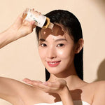 A smiling woman applying drops of Mixsoon Centella Essence directly to her forehead for hydration.